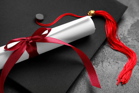 Diploma with red ribbon and graduation hat on black tableの写真素材