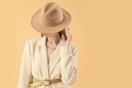 Fashionable young woman in stylish jacket and hat on beige backgroundの写真素材