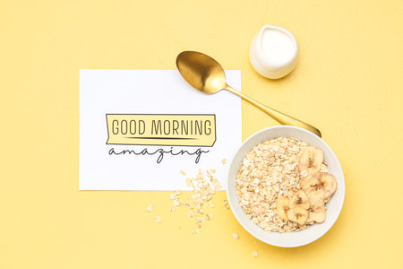 Card with text GOOD MORNING, bowl of raw oatmeal and cream on color backgroundの写真素材