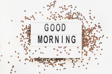 Board with text GOOD MORNING and coffee beans on light backgroundの写真素材