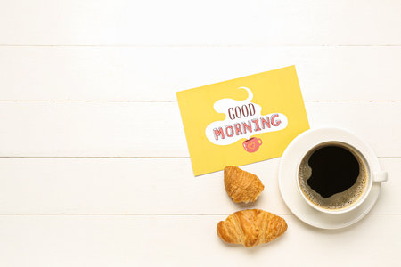 Cup of coffee, tasty croissants and card with text GOOD MORNING on light wooden backgroundの写真素材
