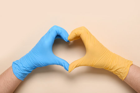 Doctor in medical gloves in colors of Ukrainian flag making heart with her hands on color backgroundの写真素材