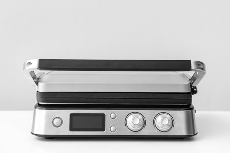 Modern electric grill with closed lid on white table against gray backgroundの写真素材