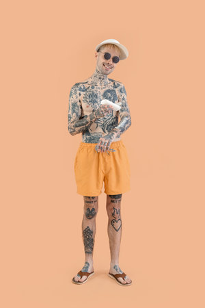 Tattooed man applying sunscreen cream on beige backgroundの写真素材