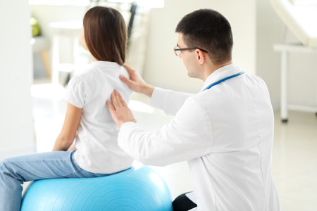 Doctor checking posture of little girl in clinicの写真素材