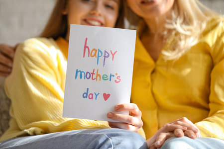 Young woman greeting her mother with card at home, closeupの写真素材