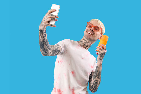 Tattooed man with sunscreen cream taking selfie on light blue backgroundの写真素材