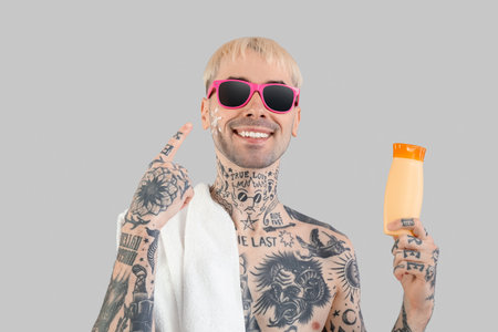 Tattooed man with sunscreen cream on light backgroundの写真素材