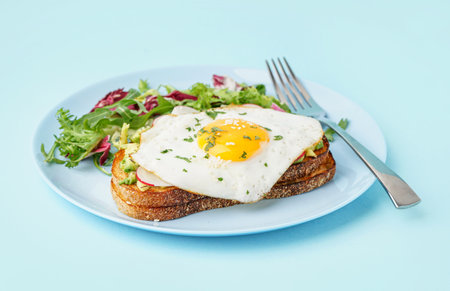Delicious sandwich with fried egg and salad on blue backgroundの写真素材