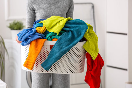Woman holding laundry basket with dirty clothes at homeの写真素材