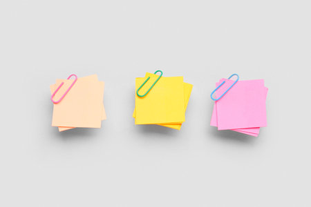 Beige, yellow and pink sticky notes with paper clips on gray backgroundの写真素材
