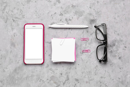 Composition with sticky notes, mobile phone and eyeglasses on grunge background