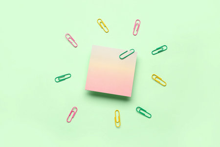 Sticky note with colorful paper clips on green background