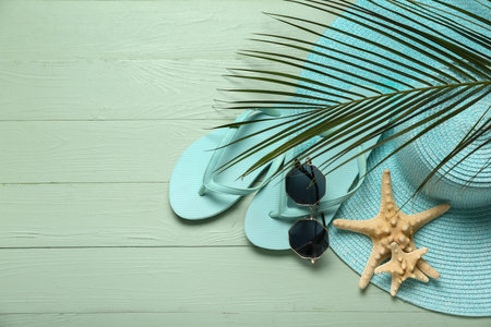 Flip-flops with sunglasses, starfishes, palm leaf and hat on green wooden background