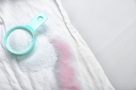 Laundry detergent with stained clothes on light background, closeup