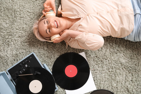 Mature woman in headphones with record player lying on carpet at home, top viewの写真素材