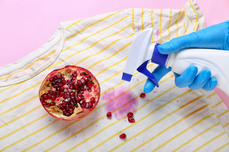 Woman spraying detergent onto stained t-shirt with pomegranate on pink background, closeupの写真素材