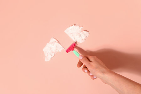 Female hand with safety razor and shaving foam on pink backgroundの写真素材