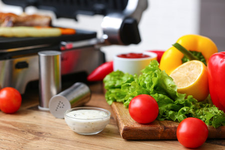 Wooden board with fresh vegetables and bowl of sauce on table in kitchenの写真素材