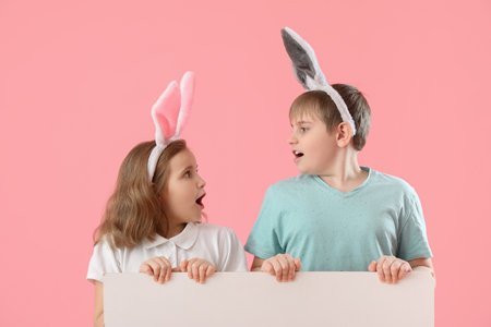 Shocked little children in bunny ears with blank poster on pink background. easter celebrationの写真素材