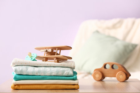 Stack of baby clothes, pacifier and wooden toys on table against color wall, closeupの写真素材