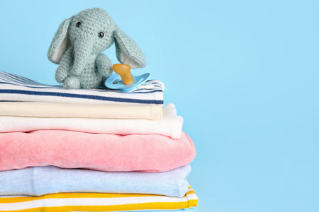 Stack of baby clothes, pacifier and toy on color background, closeupの写真素材