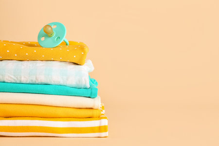 Stack of different baby clothes and pacifier on color backgroundの写真素材
