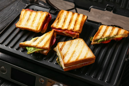 Delicious sandwiches in modern electric grill on black wooden table, closeup