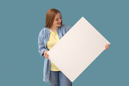 Beautiful woman with big blank poster on blue backgroundの写真素材
