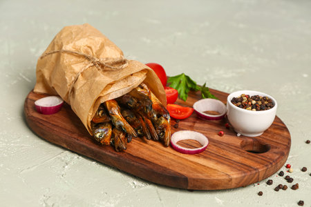 Board with tasty smoked capelin wrapped in parchment on gray background