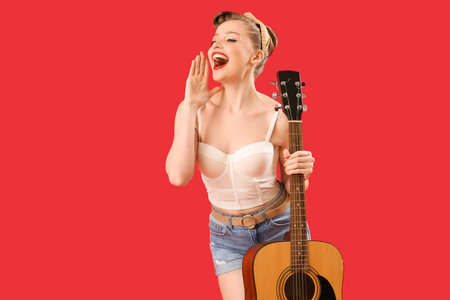 Young pin-up woman with guitar on red backgroundの写真素材