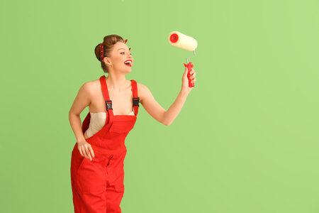 Young pin-up woman in red uniform with paint roller on green backgroundの写真素材