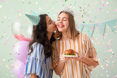 Happy young women with burger celebrating Birthday on green backgroundの写真素材