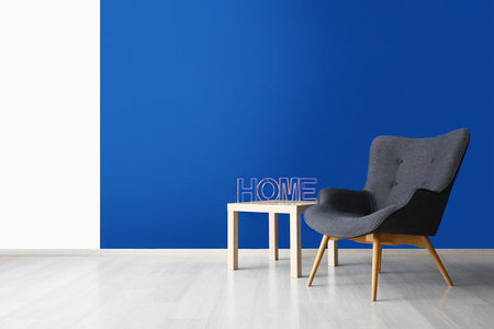 Stylish gray armchair and word HOME on table near blue wallの写真素材