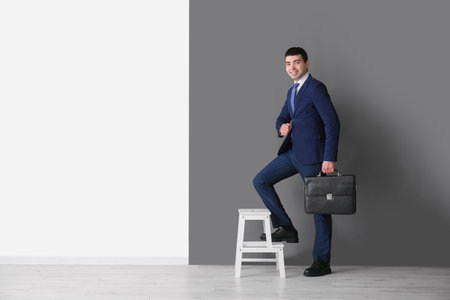 Business consultant with briefcase on stepladder near black and white wallの写真素材
