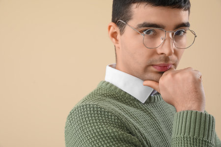 Thoughtful young man in eyeglasses on beige background, closeupの写真素材