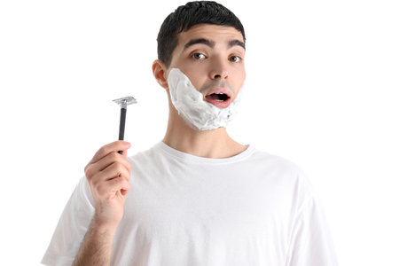 Young man shaving against white backgroundの写真素材