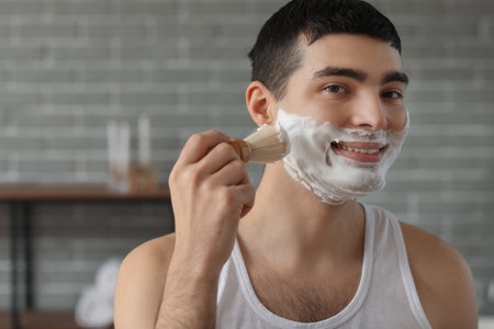 Young man applying shaving foam onto face in bathroomの写真素材
