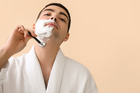 Young man shaving against beige backgroundの写真素材