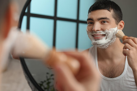 Young man applying shaving foam onto face in bathroomの写真素材