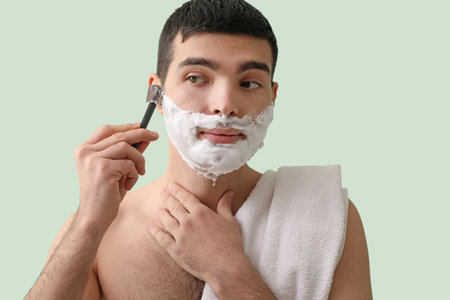 Young man shaving against green backgroundの写真素材