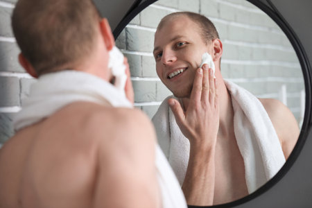 Young man shaving in front of mirror in bathroomの写真素材