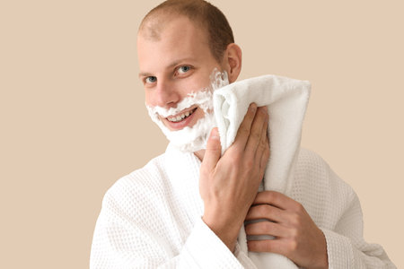 Young man shaving against beige backgroundの写真素材