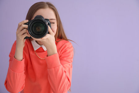 Young female photographer with professional camera on lilac backgroundの写真素材