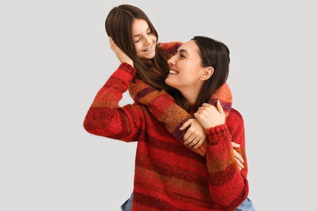 Little girl and her mother in warm sweaters hugging on gray backgroundの写真素材