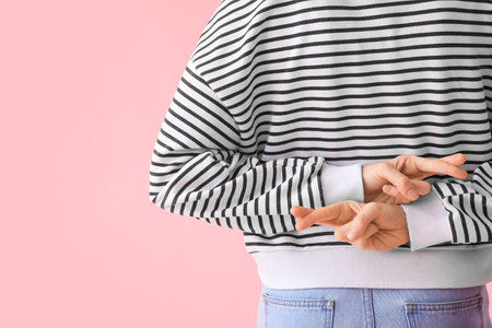 Young woman in striped sweatshirt crossing fingers on pink background, back viewの写真素材