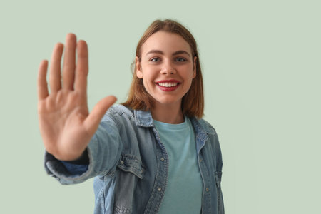 Young woman in denim shirt showing hand on green backgroundの写真素材