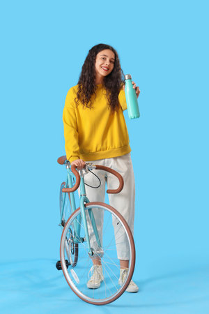 Teenage girl with bottle of water and bicycle on blue backgroundの写真素材