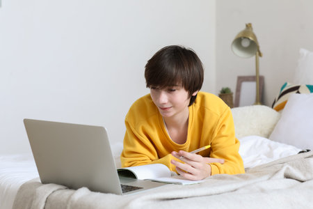 Male student with laptop studying online in bedroom