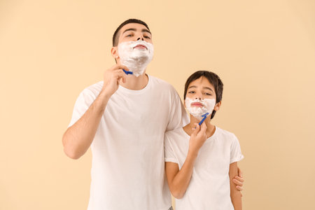 Father and his little son shaving against beige backgroundの写真素材